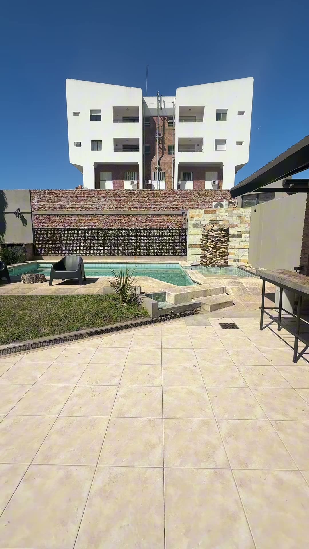 La pileta con el muro de ladrillo, el deck y el jardín alrededor